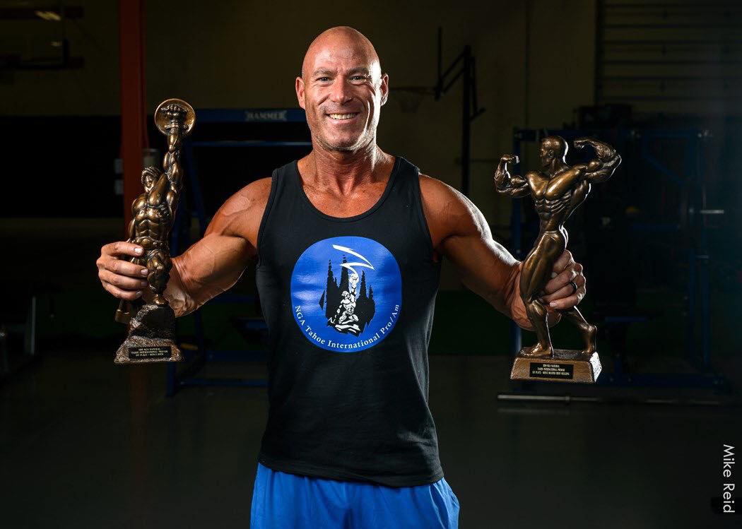 Joe Daily, certified personal trainer at Iron Body Fitness, holding bodybuilding trophies